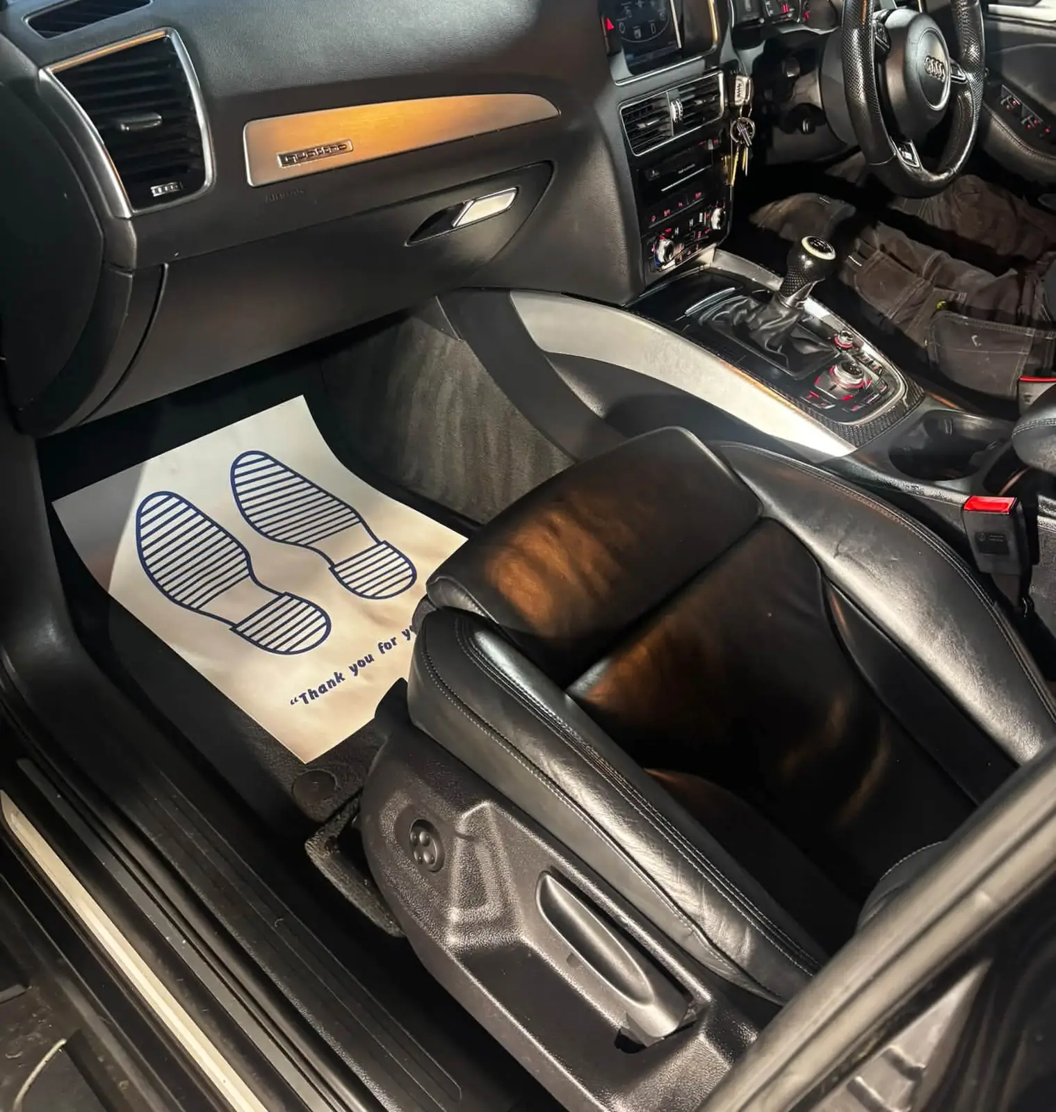 Inside a finished Audi Q5: clean dashboard, black leather seats and a paper mat in the passenger footwell